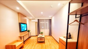 A modern hotel room with a wooden floor, a flat-screen TV mounted on the wall, a small table with two potted plants, a bench, and a wardrobe with a hanging rack. - Green Tree Inn Huangshan Yi County Xidi Hongcun (Huangshan)