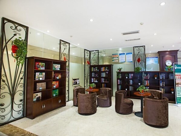 A lobby with a reception desk, multiple seating areas, and a large bookshelf filled with books.