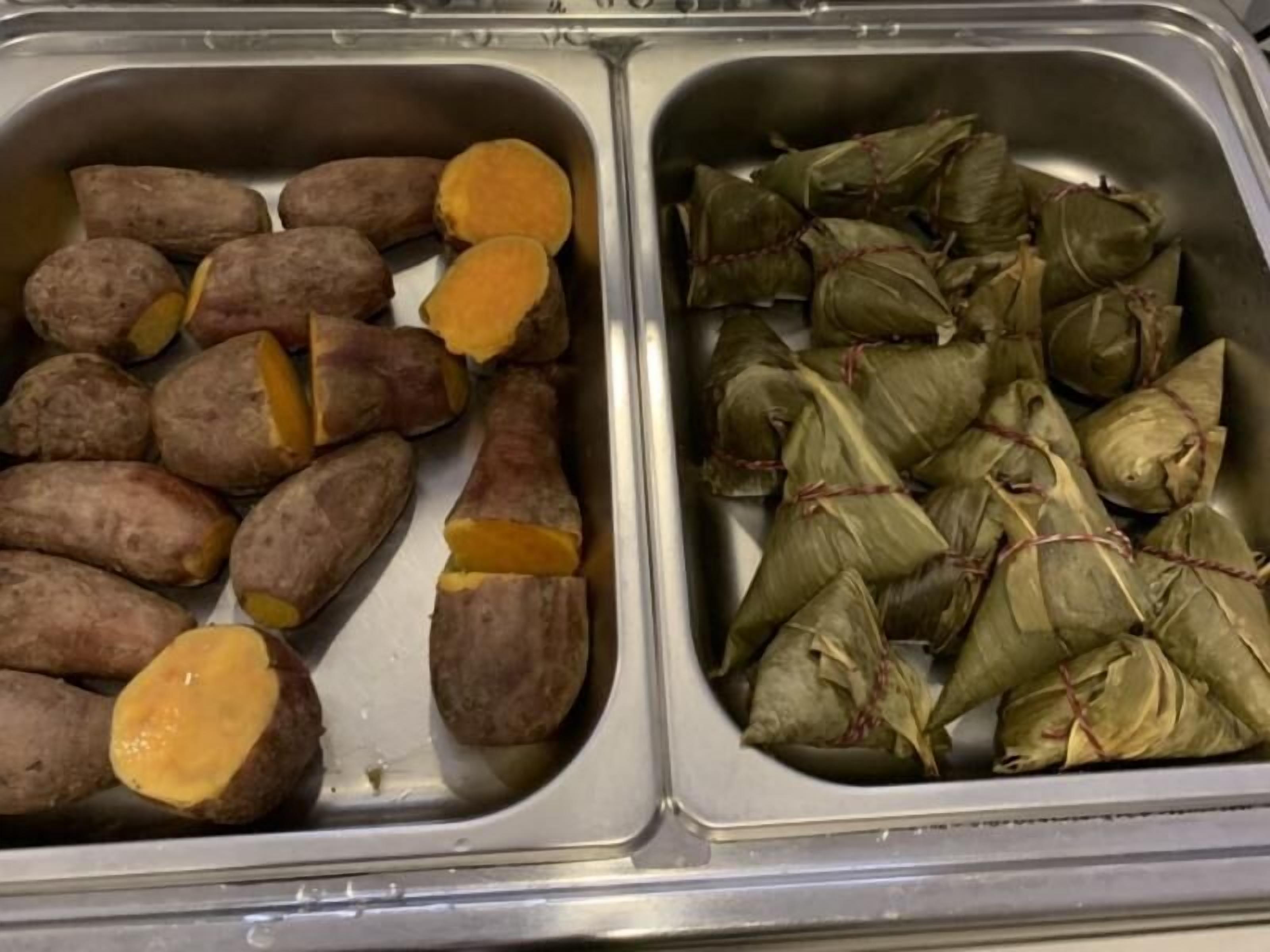 A stainless steel sink with two compartments; one contains sweet potatoes, and the other contains food wrapped in leaves.