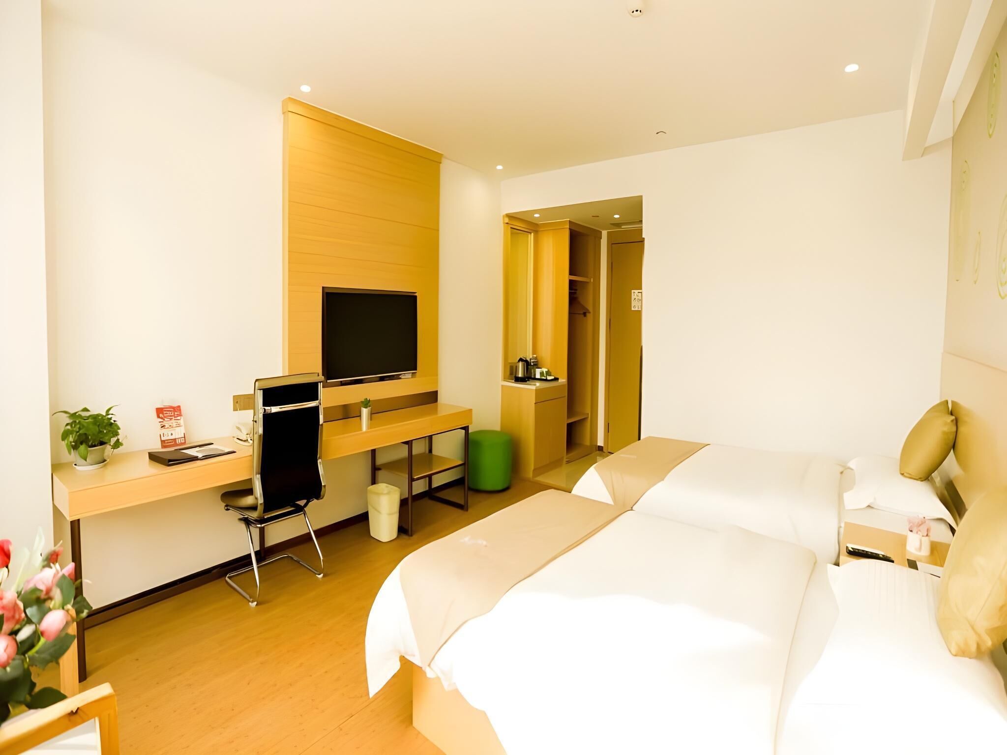A hotel room with a wooden desk, a television, a bed, and a green trash bin.