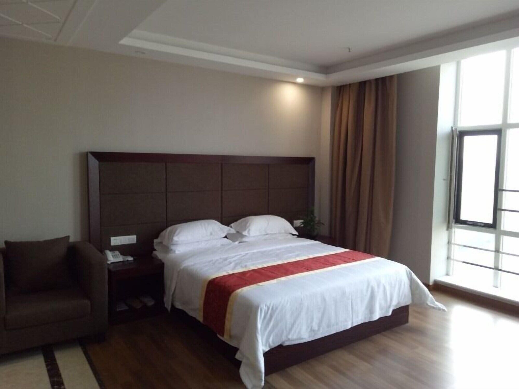 A hotel room with a large bed, a nightstand, a chair, and a window with curtains.