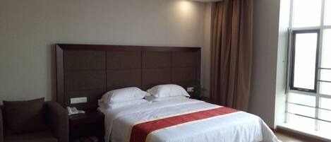A hotel room with a large bed, a nightstand, a chair, and a window with curtains.