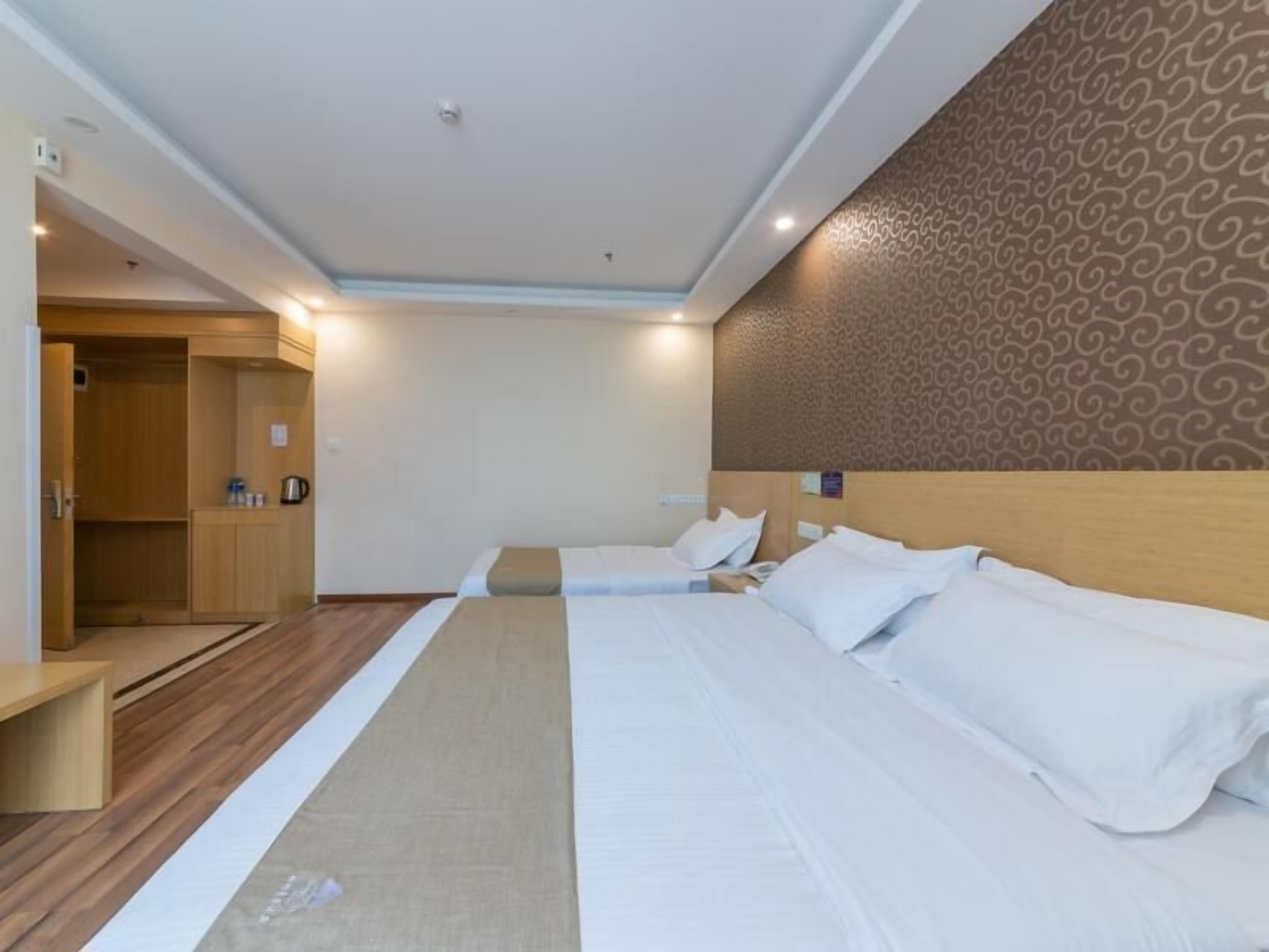 A hotel room with two beds, a wooden wardrobe, a small kitchenette, and a patterned wall.