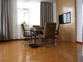 A conference room with a round table, four chairs, a TV on the wall, and a window with curtains.