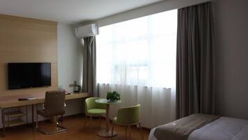 A hotel room with a bed, a desk, a chair, a TV, and a window with curtains.