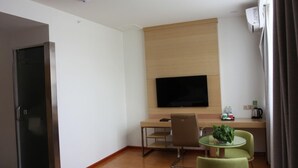 Una habitación de hotel con cama, escritorio y silla, televisor montado en la pared y una pequeña mesa con sillas.
