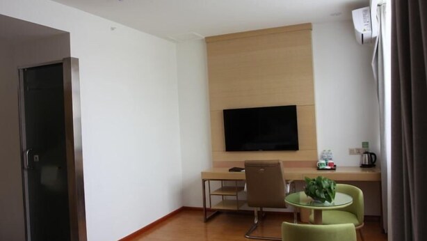 Habitación de hotel con cama, escritorio con silla, televisor montado en la pared y una pequeña mesa con sillas.