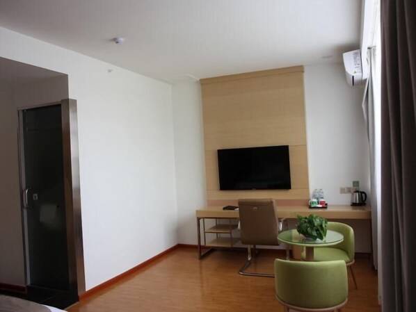Habitación de hotel con cama, escritorio con silla, televisor montado en la pared y una pequeña mesa con sillas.
