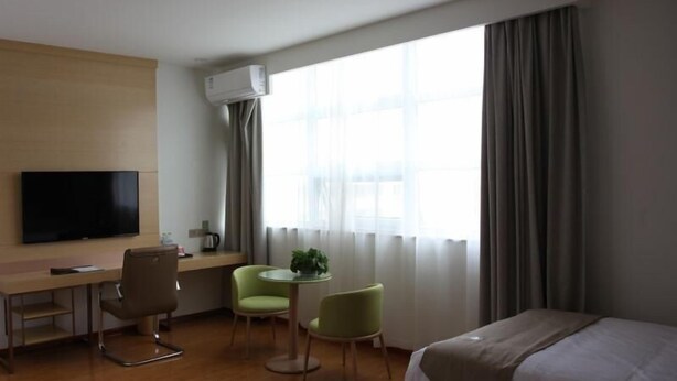 Habitación de hotel con cama, escritorio, silla, televisor y ventana con cortinas.