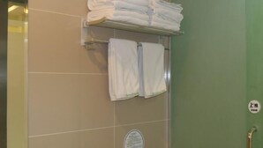 Un baño con azulejos color beige, un perchero con toallas dobladas, un secador de manos y una puerta verde con baranda.