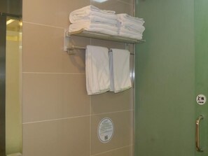 Un baño con azulejos color beige, un perchero con toallas dobladas, un secador de manos y una puerta verde con baranda.