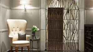 A room with a tufted armchair, a small side table with a vase of flowers, and a decorative metal gate. - Las Alcobas A Luxury Collection Hotel Mexico City (Mexico City)