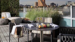 A rooftop terrace with a round table set for two, featuring a bottle, glasses, and a plate of fruit. There are cushioned chairs and a sofa with striped cushions. - Las Alcobas A Luxury Collection Hotel Mexico City (Mexico City)