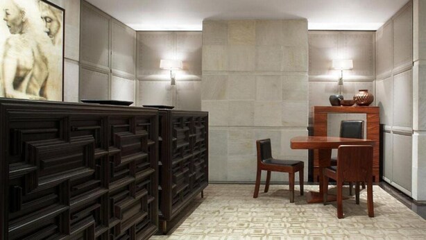 A modern room with a geometric patterned floor, a dark wooden cabinet, a dining table with chairs, and wall-mounted lamps. - Las Alcobas A Luxury Collection Hotel Mexico City (Mexico City)