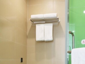 Un baño con baldosas color beige, una puerta de ducha de vidrio y un perchero con dos toallas.