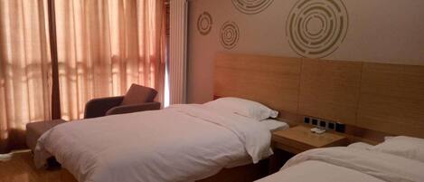 Ein Hotelzimmer mit zwei Betten, einem Sessel, einem Nachttisch und einem Fenster mit Vorhängen.