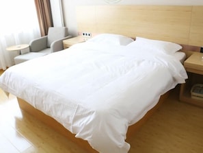 Una habitación de hotel con una cama grande, una mesita de noche, una silla y una pequeña mesa.