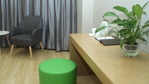 A modern room with a grey armchair, a wooden desk, a green stool, a potted plant, and a grey curtain. - Greentree Inn Lvliang Xiaoyi City Fuqian Street Hotel (Lvliang)