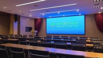 A conference room with a large screen displaying 'GreenTree Inn' branding, rows of chairs, and a wooden table.