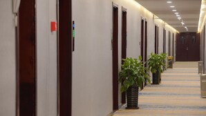Pasillo de hotel con puertas, plantas en macetas y suelo alfombrado.