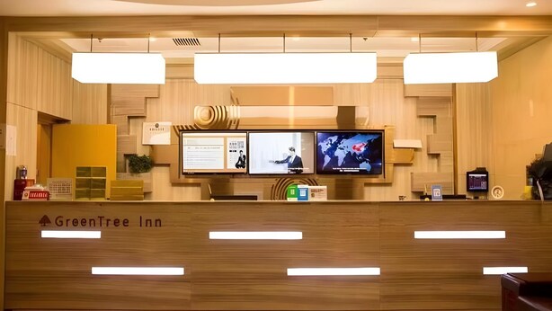 A reception desk with a wooden finish, a digital screen displaying information, and a world map. - Greentree Inn Qinhuangdao Lulong County North Gate Road (Qinhuangdao)