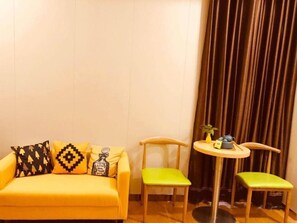 A yellow sofa with patterned cushions, two green chairs, and a small round table with a plant and a bottle. - Greentree Inn Qinhuangdao Lulong County North Gate Road (Qinhuangdao)