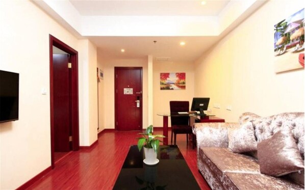 Quarto de hotel com piso de madeira, sofá, televisão, escrivaninha com computador e porta.
