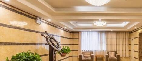 A spacious lobby with a chandelier, a ship's wheel, and two potted plants.