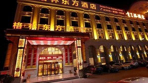 Un hôtel au style architectural traditionnel, avec une entrée imposante surmontée d’un auvent rouge et agrémentée d’une enseigne lumineuse.