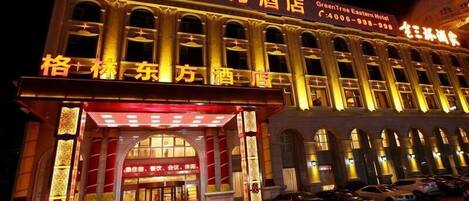 A hotel with a traditional architectural style, featuring a prominent entrance with a red awning and illuminated signage.
