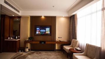 Habitación de hotel con televisor de pantalla plana montado en la pared, zona de estar con dos sillones, una mesita y un tapete decorativo.