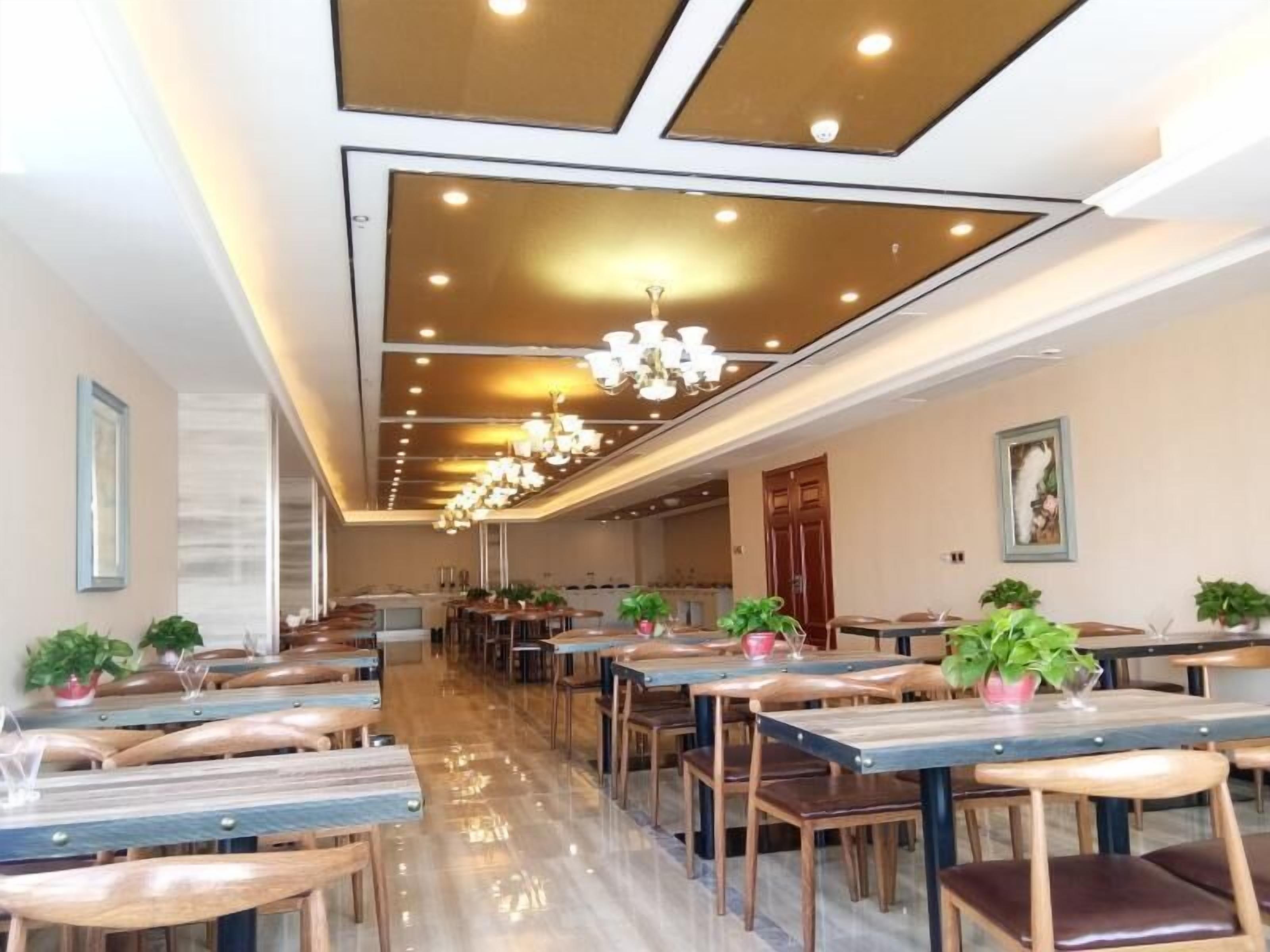 A spacious dining area with multiple tables and chairs, a modern chandelier, and potted plants.