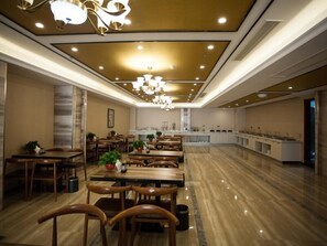 Un comedor amplio con mesas y sillas de madera, una estación de servicio central y una lámpara de araña moderna.