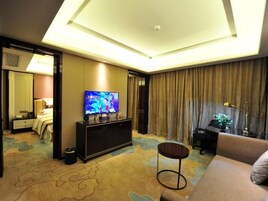 Habitación de hotel con un televisor de pantalla plana grande sobre un mueble, un sofá, una mesita redonda y una lámpara del techo.