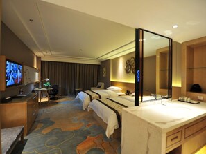 A hotel room with a large bed, a desk with a computer, a TV, and a bathroom with a mirror and sink.