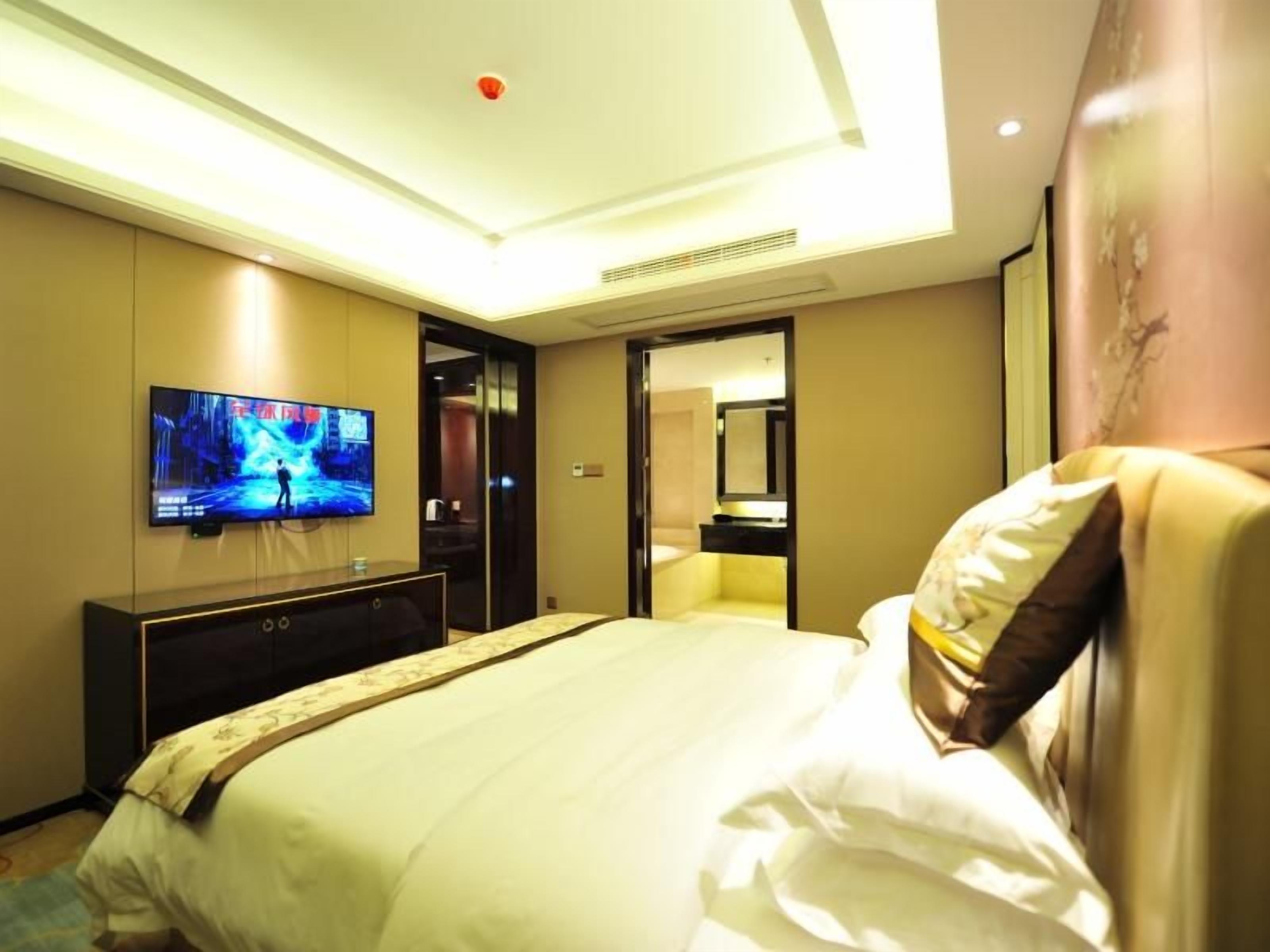Quarto de hotel com uma cama grande, televisão de tela plana na parede, mesa de cabeceira e porta para o banheiro.