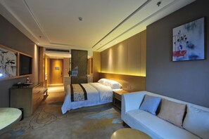 A hotel room with a bed, a sofa, a desk, and a TV.