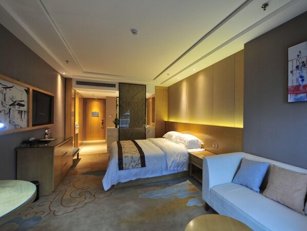 A modern hotel room with a large bed, a sofa, a desk, and a television.
