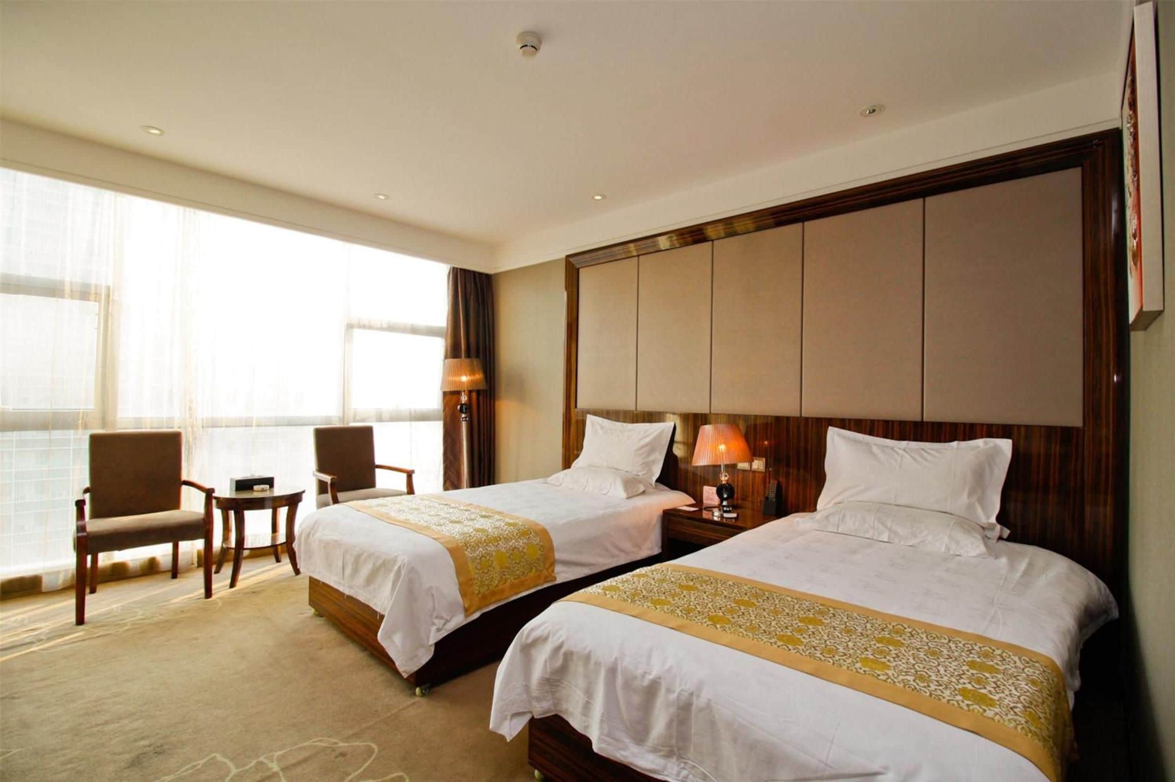 A hotel room with two beds, a large window with curtains, a desk, and a chair.