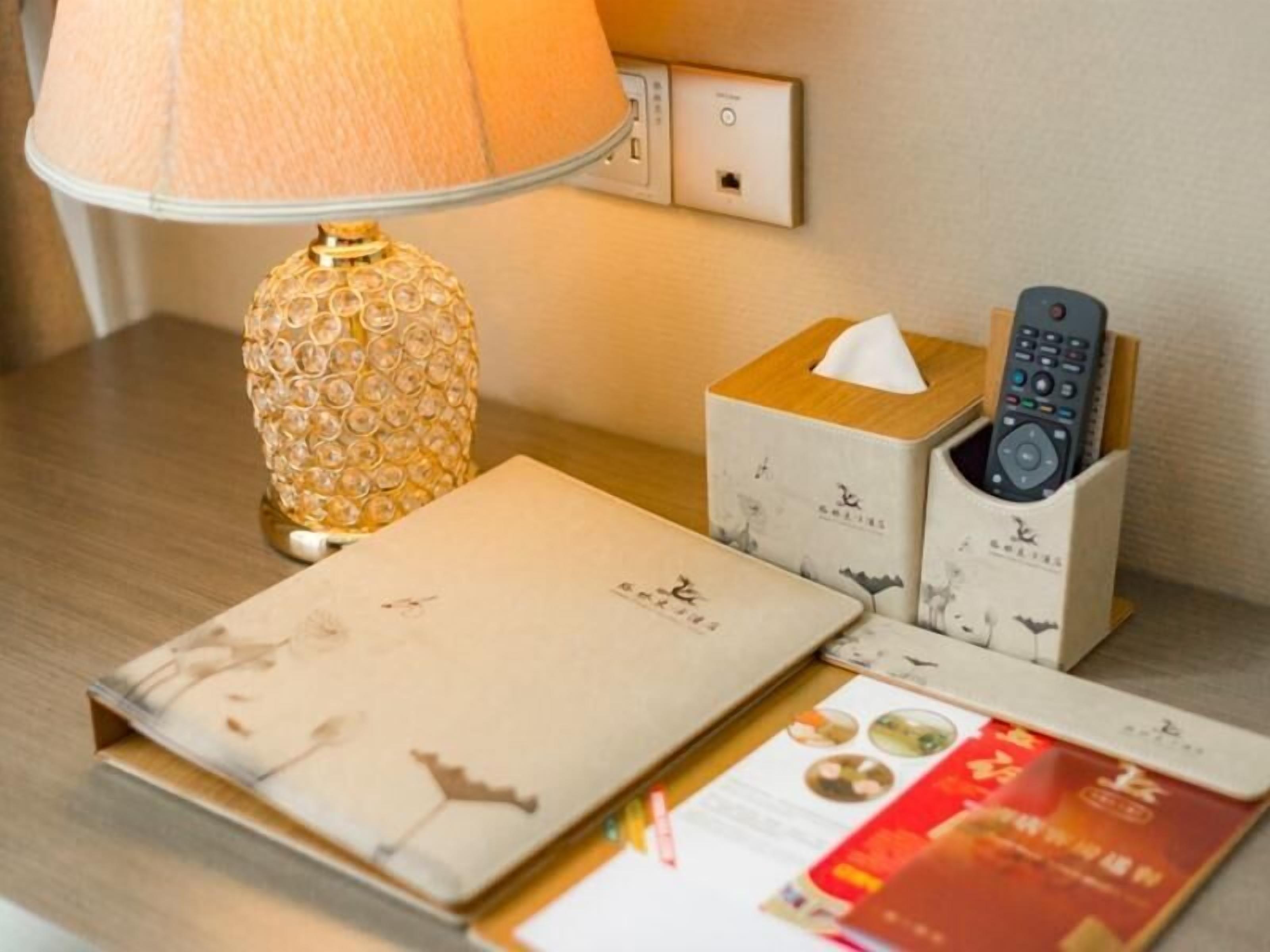 A bedside table with a lamp, a tissue box, a remote control holder, and a menu.