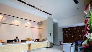 Un espace d’accueil moderne comprenant un comptoir de réception, une réceptionniste, un coin salon avec une bibliothèque et une plante décorative.