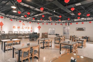 A restaurant with tables and chairs, red lanterns hanging from the ceiling, and a wall with Chinese characters.