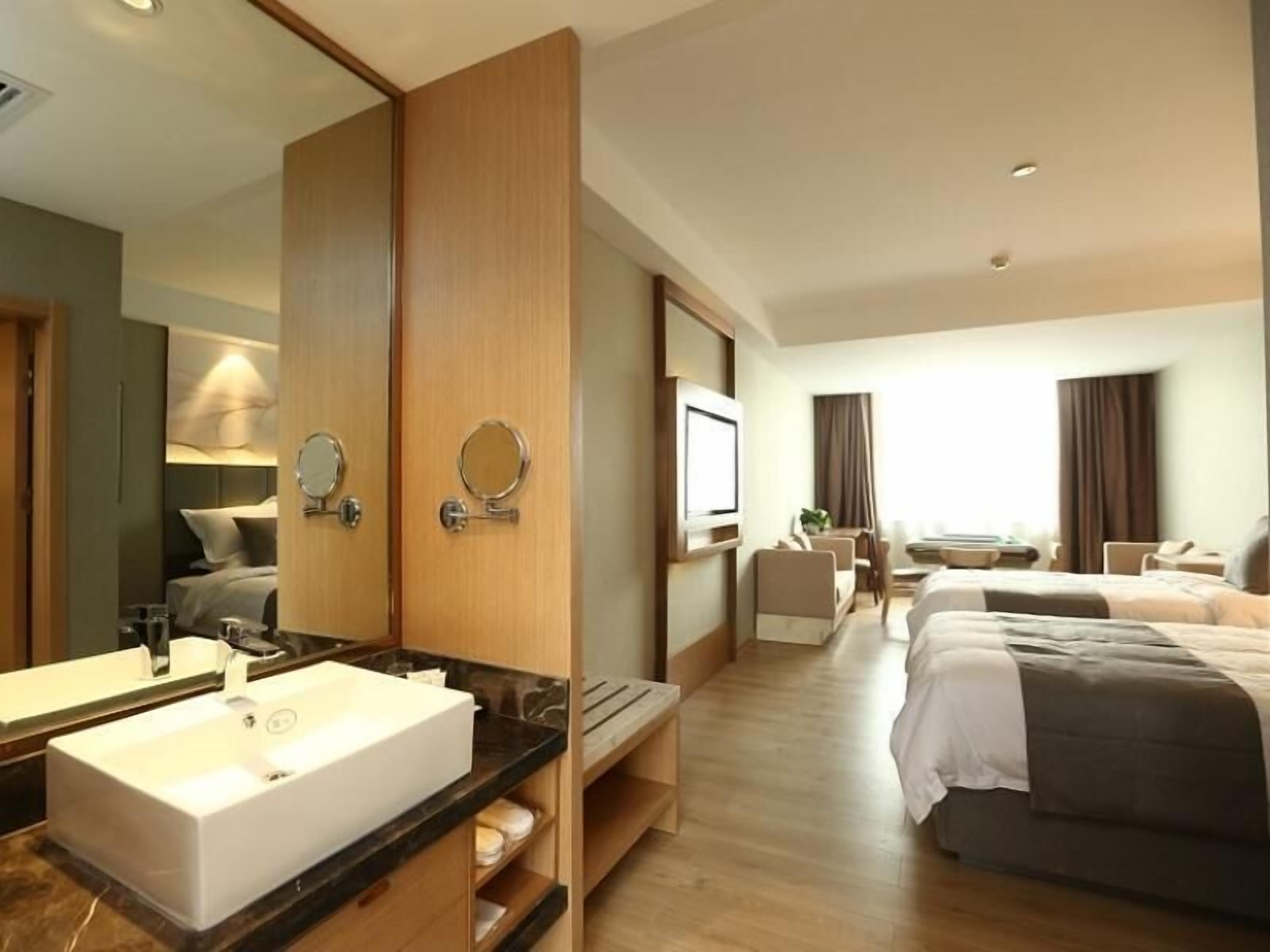 Une chambre d’hôtel avec un grand miroir, un lavabo blanc, un lit, une télévision et un bureau avec une chaise.