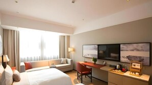 Ett hotellrum med två sängar, ett skrivbord, en tv och ett fönster med gardiner.