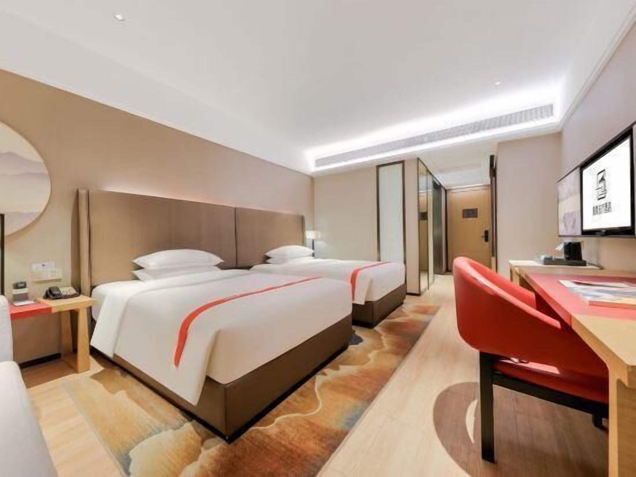 A hotel room with two beds, a desk, a chair, a TV, and a mirror.
