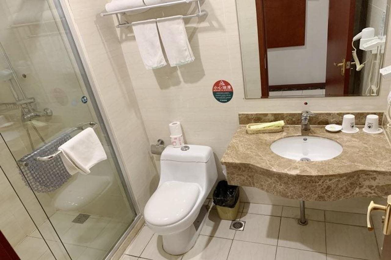 A bathroom with a glass shower enclosure, a toilet, a sink with a marble countertop, and a mirror.