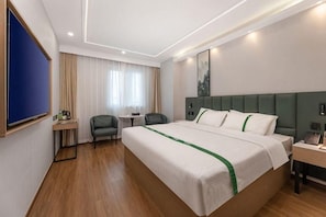 Une chambre d’hôtel avec un grand lit, un bureau, une chaise, une petite table et une fenêtre avec des rideaux.