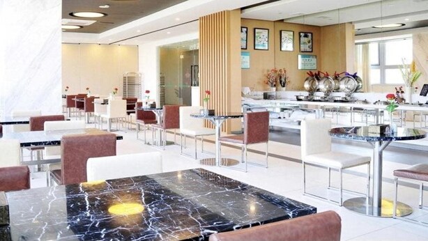 Un moderno vestíbulo de hotel con mesas y sillas de encimera de mármol, una zona de recepción con mostrador y obras de arte enmarcadas en las paredes.