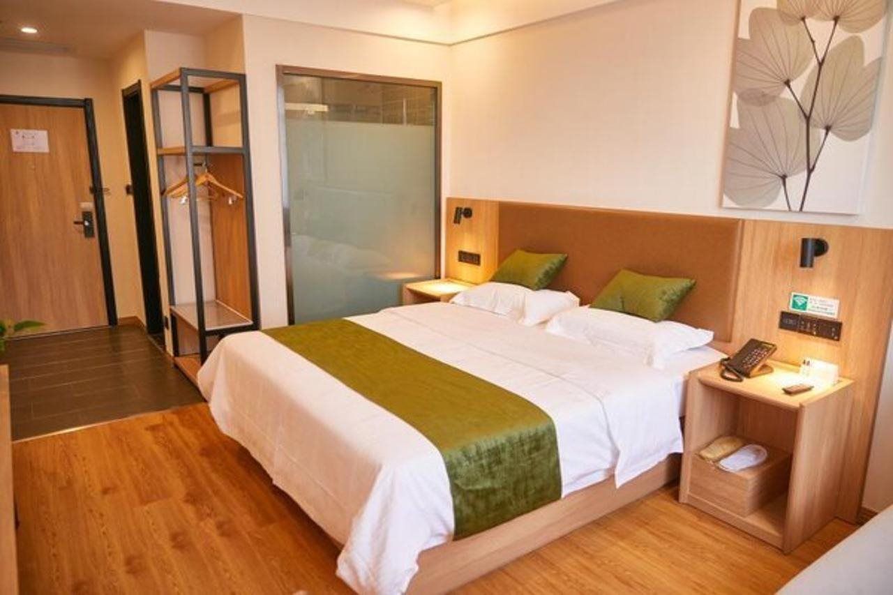 A hotel room with a bed, a bedside table with a lamp, a wall-mounted phone, and a door with a hanging coat rack.