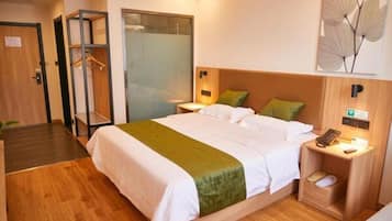 A hotel room with a bed, a bedside table with a lamp, a wall-mounted phone, and a door with a hanging coat rack.